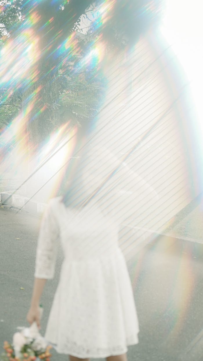 Artistic shot of a woman in a white dress with blurred rainbow flare creating a mystical ambiance.